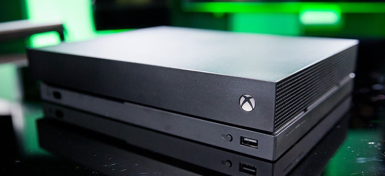 xbox one x console in black on top of a black surface with green blurry lights